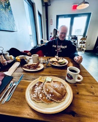 a man sitting at a table with a plate of pancakes and coffee